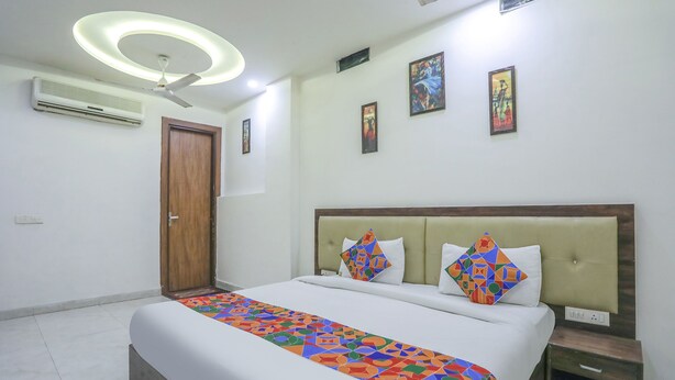 A hotel room with a bed, a ceiling fan, an air conditioner, a wooden door, and a nightstand. - Fabhotel Shriansh (Agra)