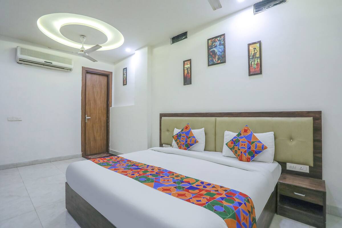 A hotel room with a bed, a ceiling fan, an air conditioner, a wooden door, and a nightstand.
