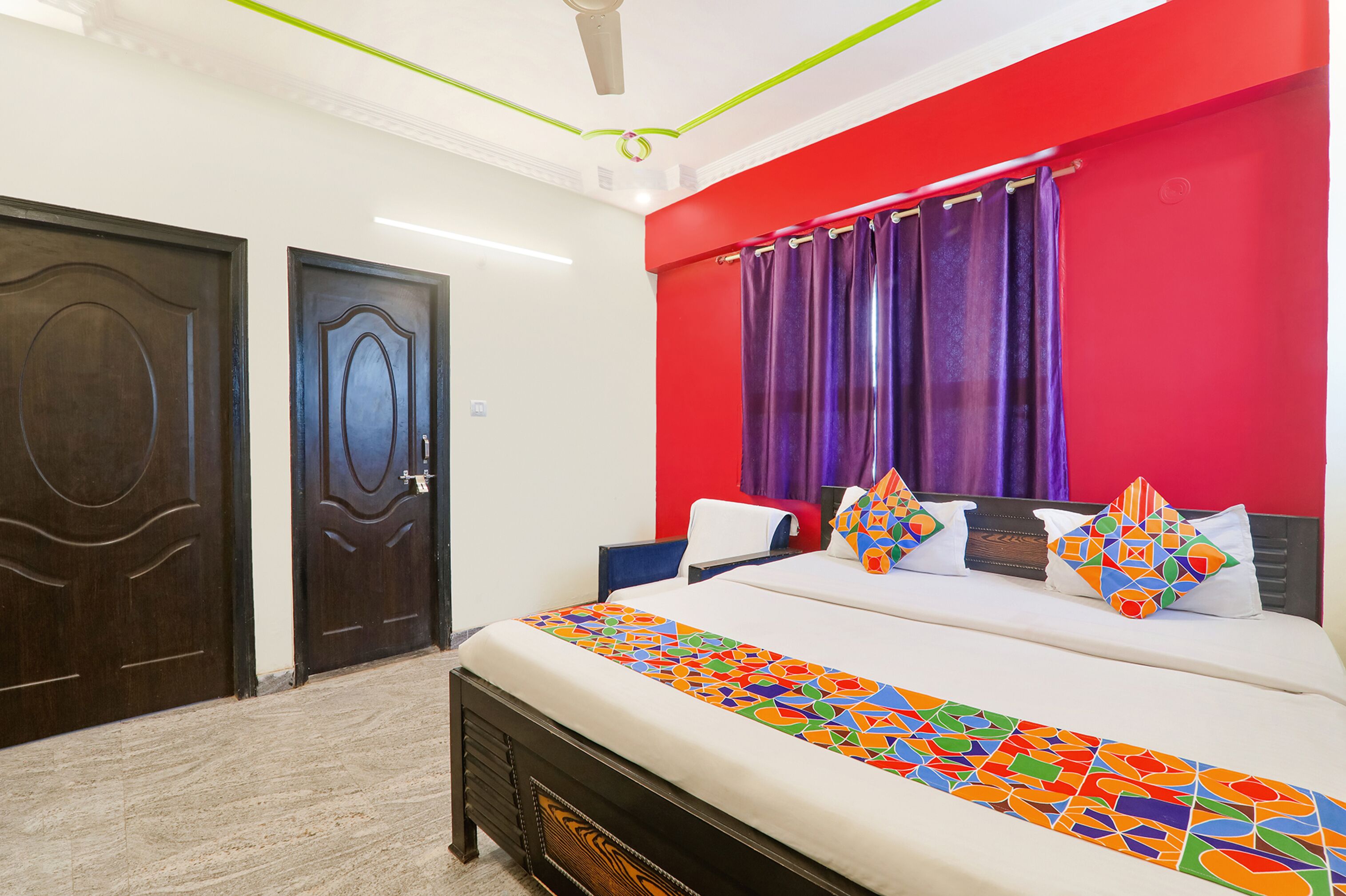 A hotel room with a bed, a headboard, a window with purple curtains, and two doors.