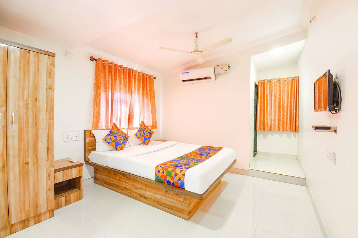 A bedroom with a wooden bed frame, white bedding, an air conditioning unit, and a ceiling fan.