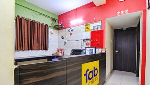 Un comptoir d’accueil d’hôtel avec un comptoir en bois, une enseigne indiquant « fab hotels », et un mur rouge orné d’une horloge.