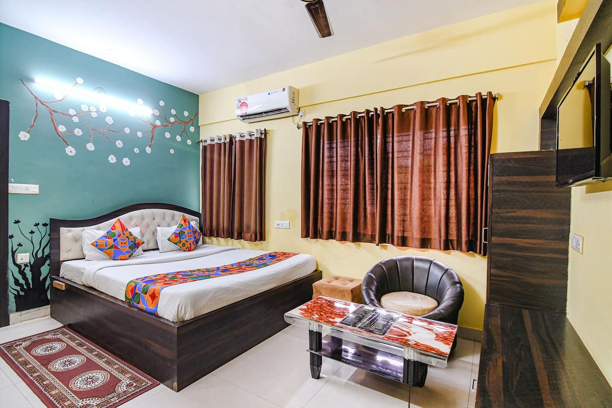 A bedroom with a bed, a chair, a table, curtains, an air conditioner, and a wall with a tree mural.