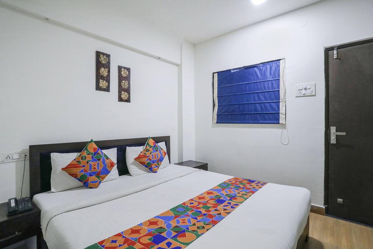 A hotel room with a large bed, two decorative wall pieces, a window with blue blinds, and a door.