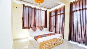 A bedroom with a wooden bed, white bedding, and curtains. - Fabexpress Prajakta Holiday Inn (Mahabaleshwar)