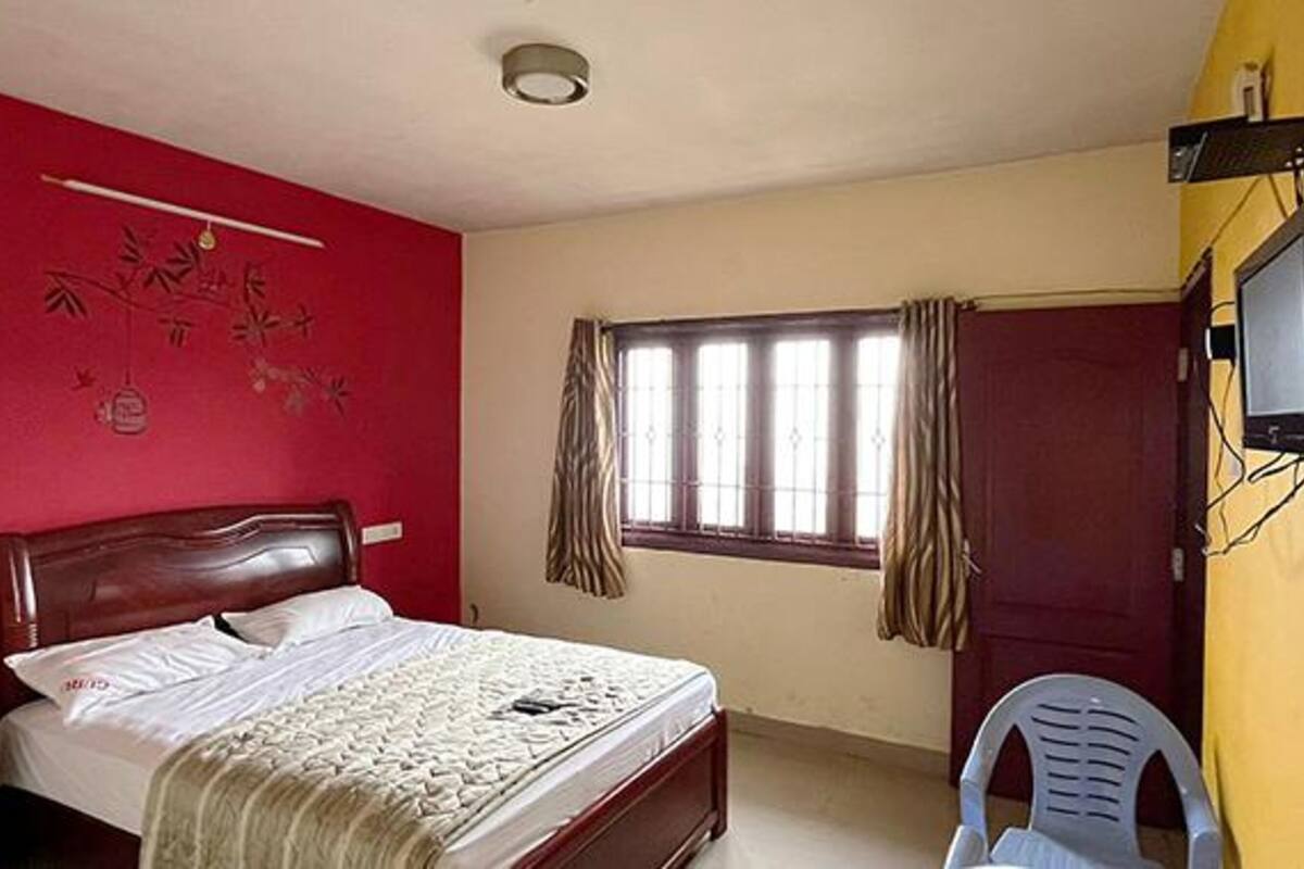 A bedroom with a bed, a TV mounted on the wall, a window with curtains, and a chair.