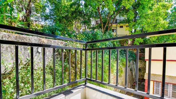 A balcony with a metal railing overlooking a lush garden and a building in the background. - Fabhotel Pacific Inn (Dehradun)