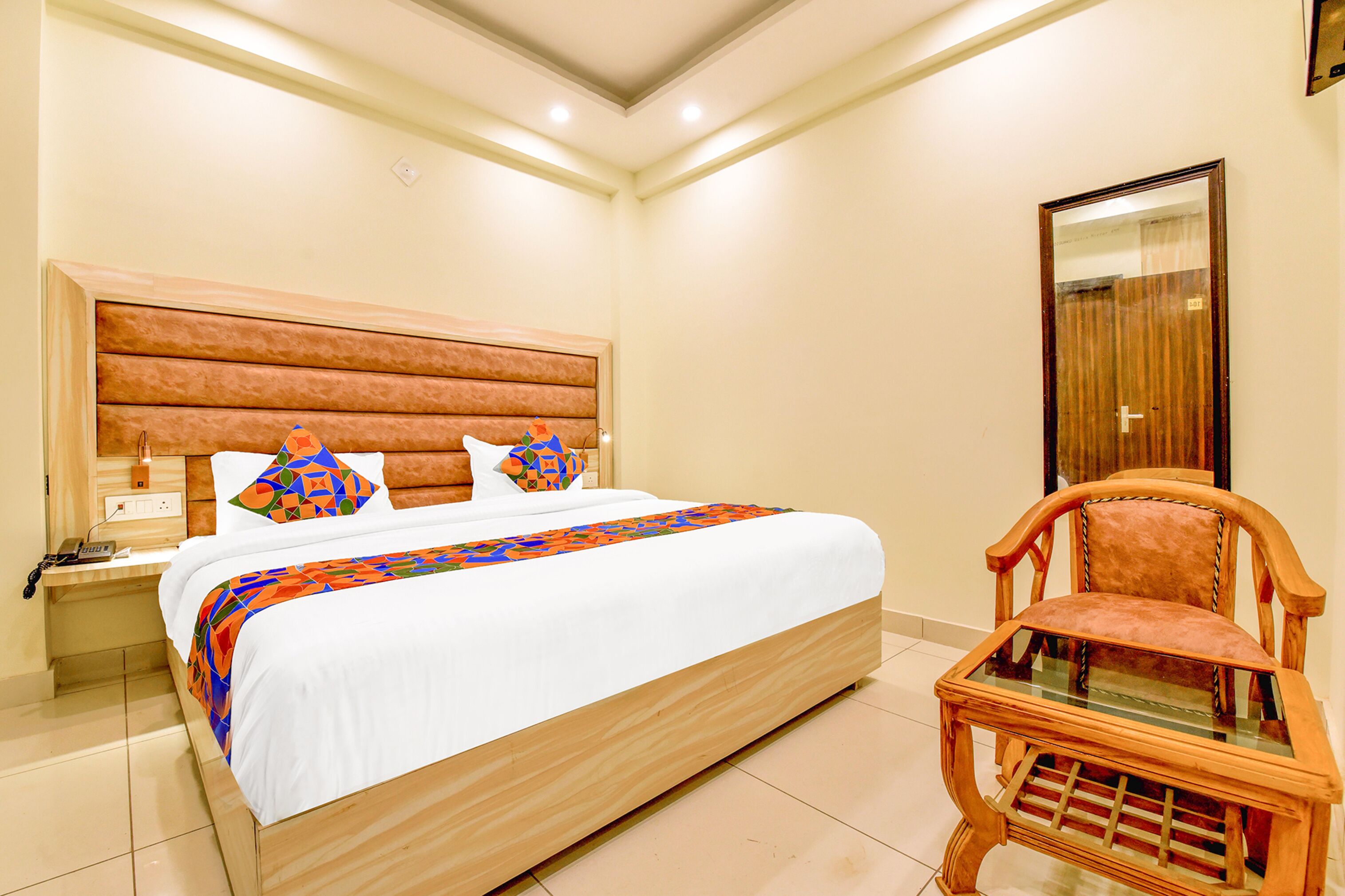 A neatly made bed with a patterned bedspread, a wooden headboard, and a nightstand with a phone.