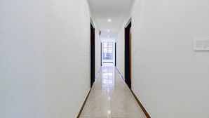 A long, narrow hallway with white walls and a shiny tiled floor, leading to a bright room with a large window. - Fabhotel Pacific Inn (Dehradun)