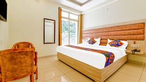 A hotel room with a large bed, a wooden headboard, a bedside table with a phone, and a chair. - Fabhotel Pacific Inn (Dehradun)