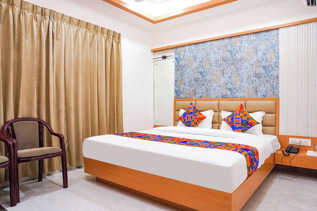 Une chambre à coucher comprenant un lit, une chaise, une table de chevet et un mur orné d’un motif décoratif.