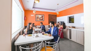 A dining area with a white table and chairs, a kitchen area with a counter and cabinets, and a painting on the wall.