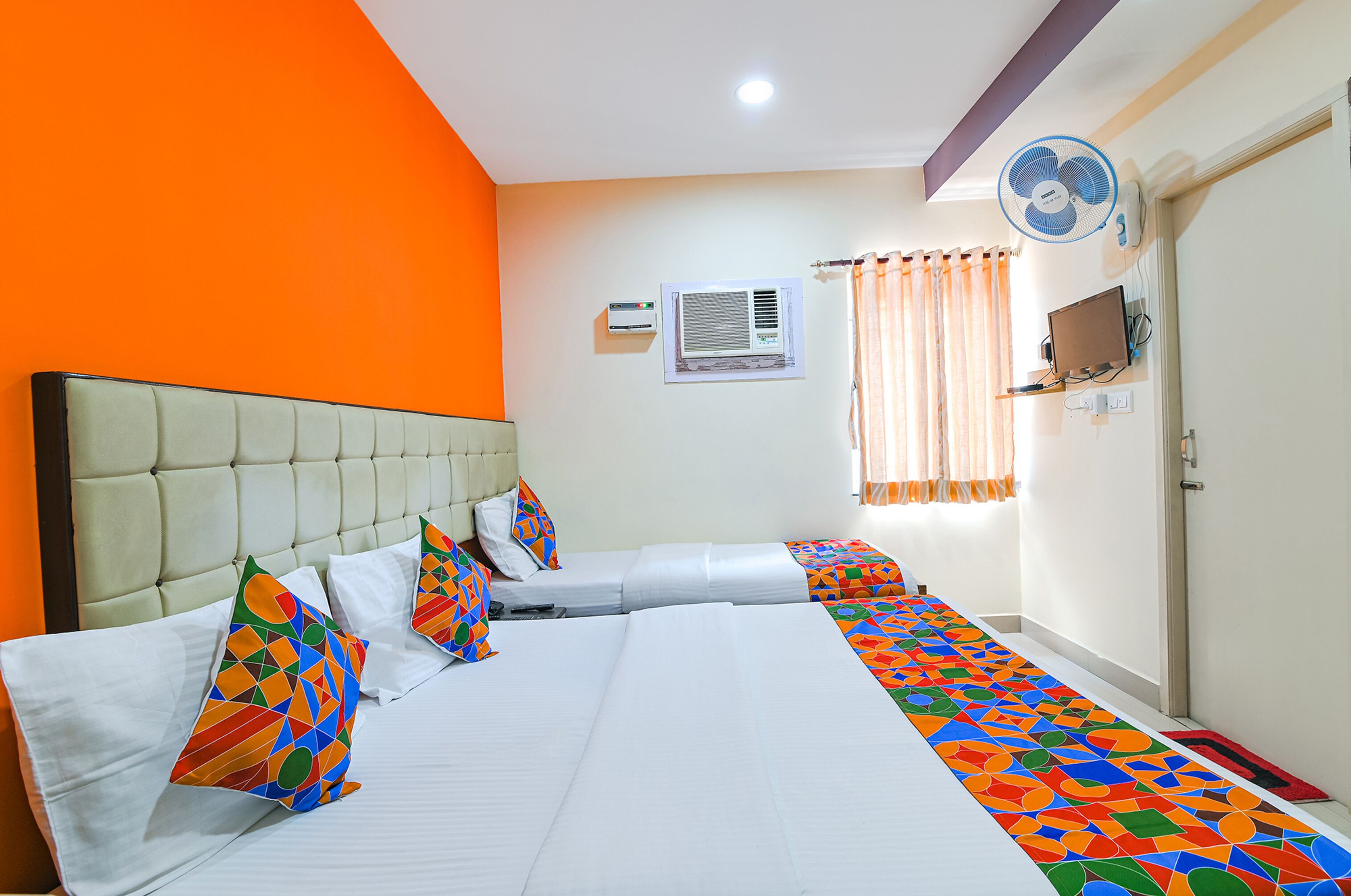 Een hotelkamer met een groot bed, een airconditioning, een televisie en een raam met gordijnen.