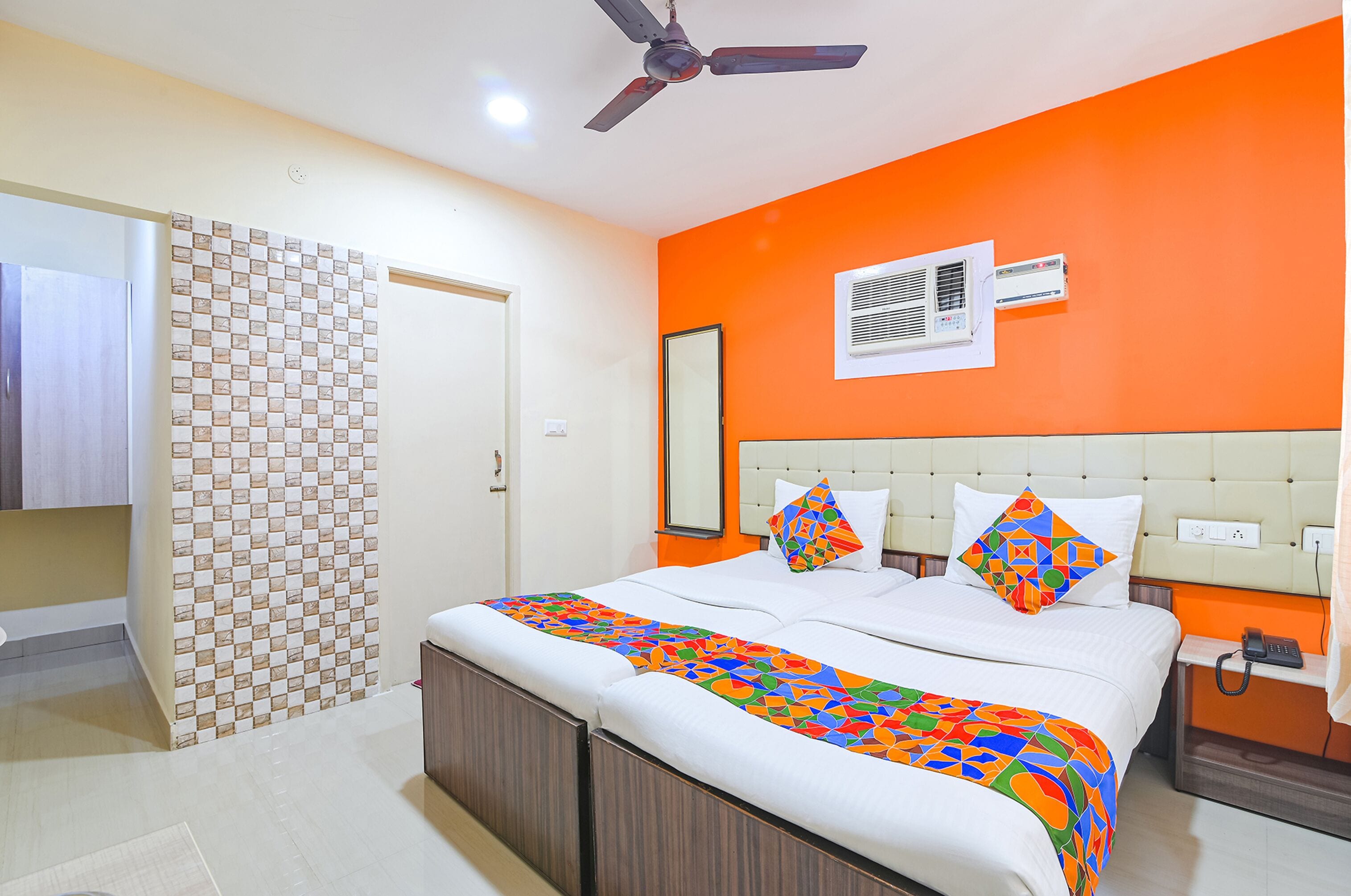 A hotel room with a bed, a ceiling fan, an air conditioning unit, and a bedside table with a phone.