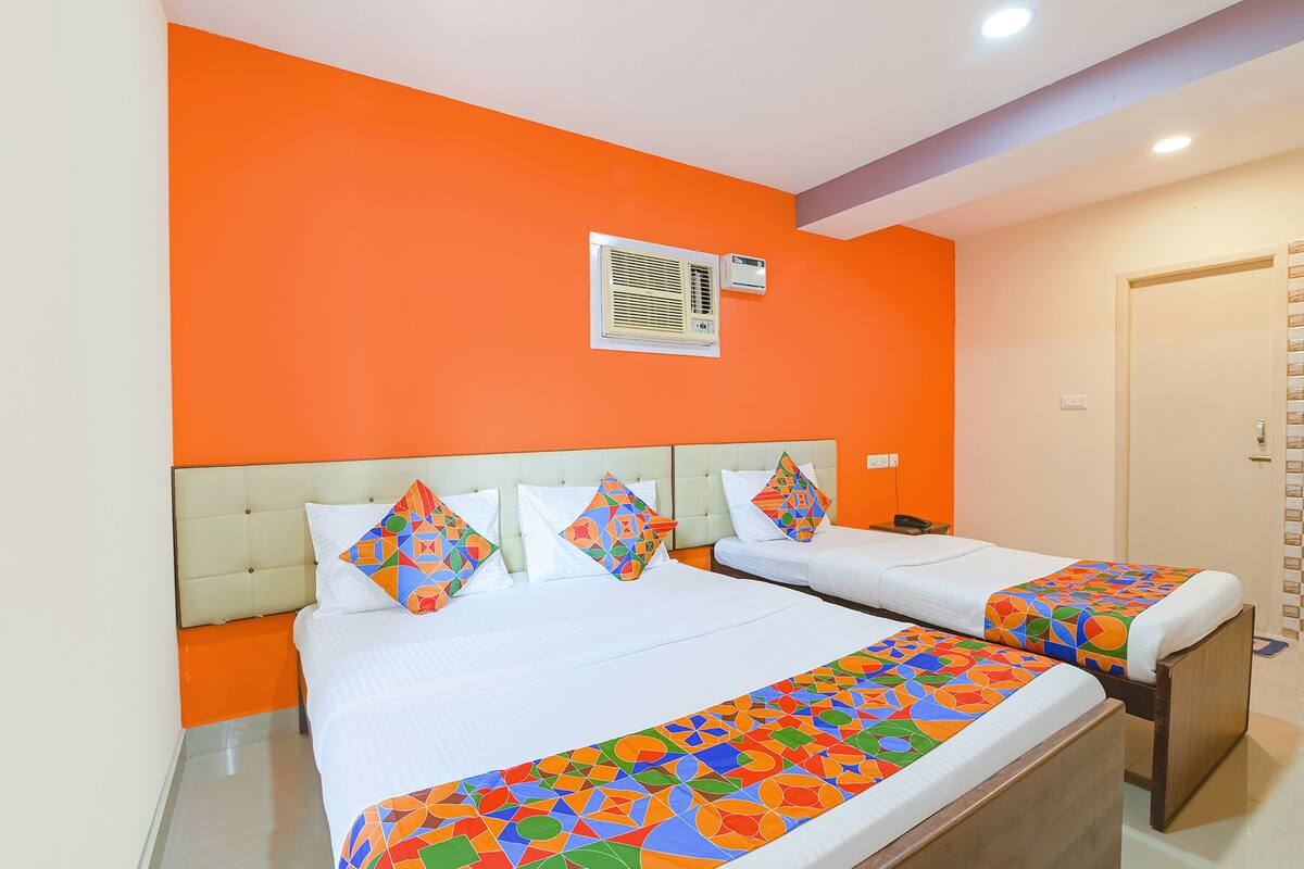 Een hotelkamer met twee bedden, oranje wanden, een wit hoofdeinde en een bedspread met een patroon.
