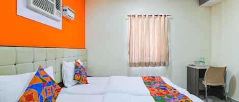 A hotel room with two beds, a window with curtains, a small desk with a chair, and an air conditioning unit on the wall.