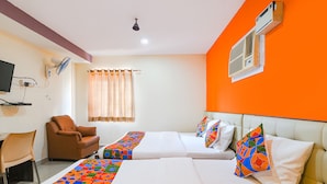 A hotel room with two beds, a chair, a desk, a TV, and an air conditioning unit.