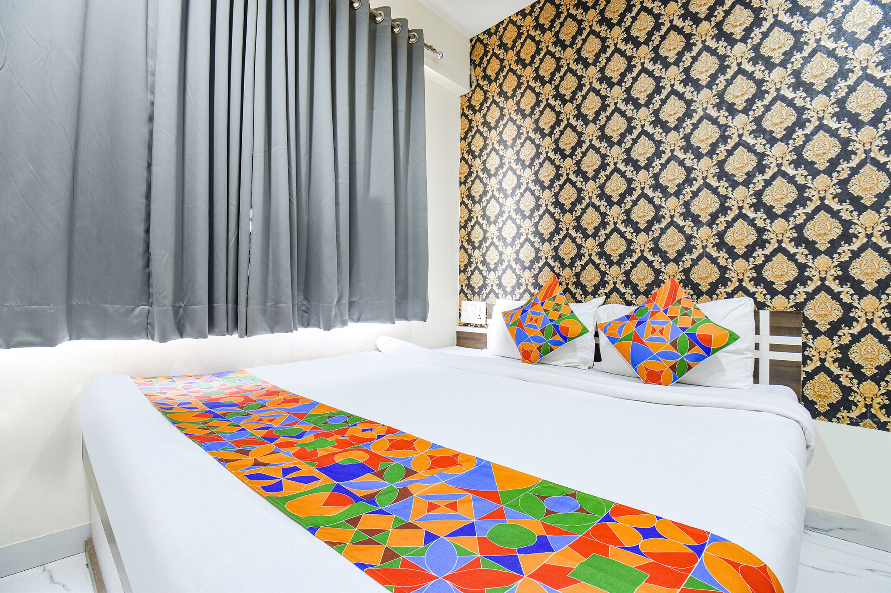 A hotel room with a bed, curtains, patterned wallpaper, and a colorful bed runner.