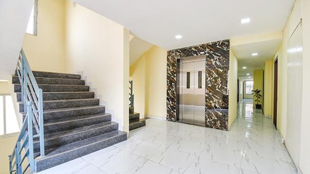 A modern interior with a marble staircase, a glass elevator, and a hallway with a yellow wall.