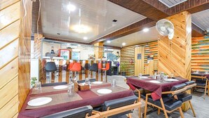 A restaurant with wooden walls and ceiling, tables with red tablecloths, and a counter area.