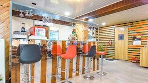 A bar area with four stools, a counter with a beverage dispenser, and a wooden wall with a slatted design.