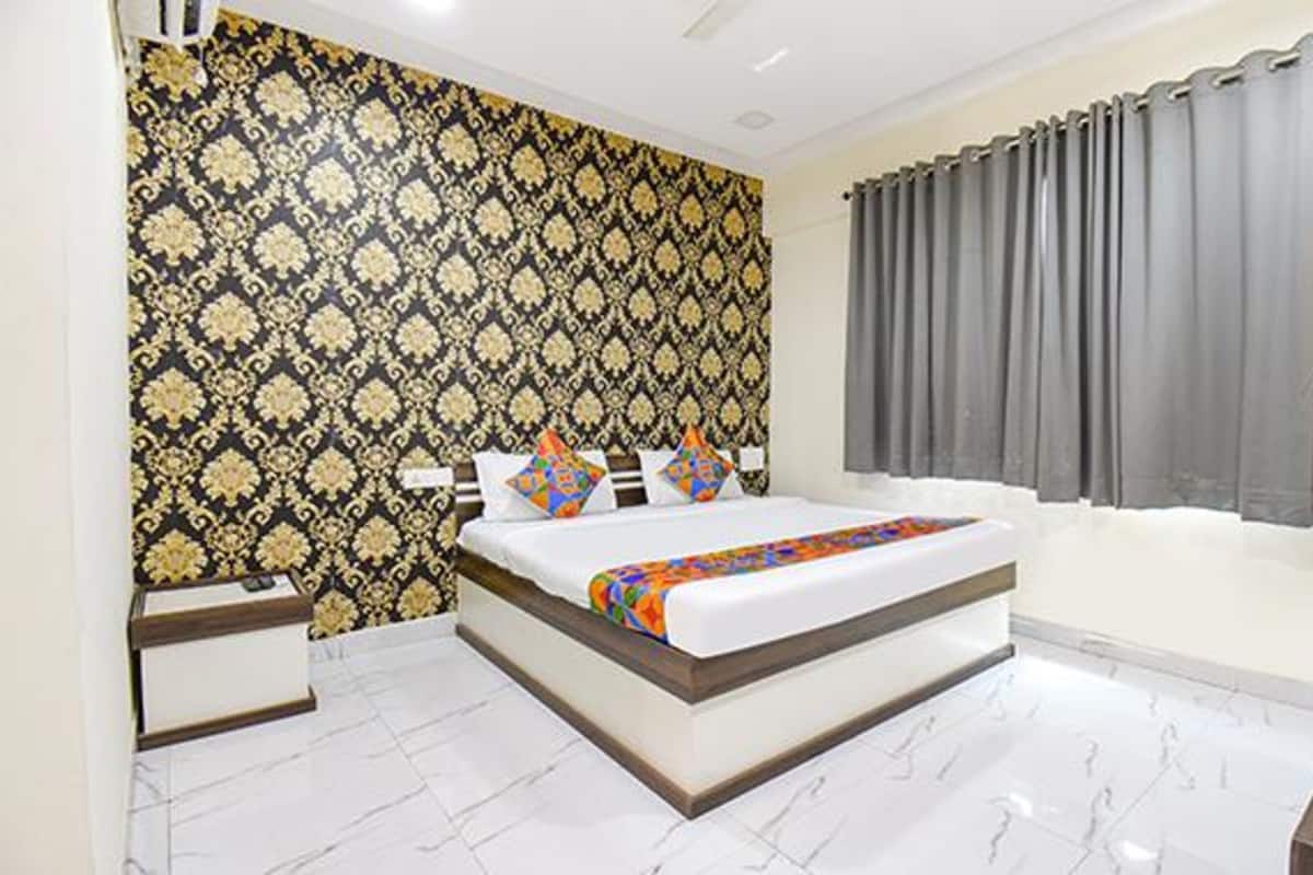 A bedroom with a patterned wallpaper, a bed with a colorful blanket, a window with grey curtains, and a white tiled floor.
