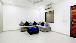 Uma sala de estar moderna com um sofá seccional cinza, um banquinho azul, um ventilador de teto e um aparelho de ar condicionado.