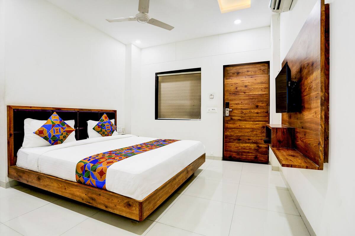 Quarto moderno com estrutura de cama de madeira, ventilador de teto, TV fixada na parede e porta de madeira.