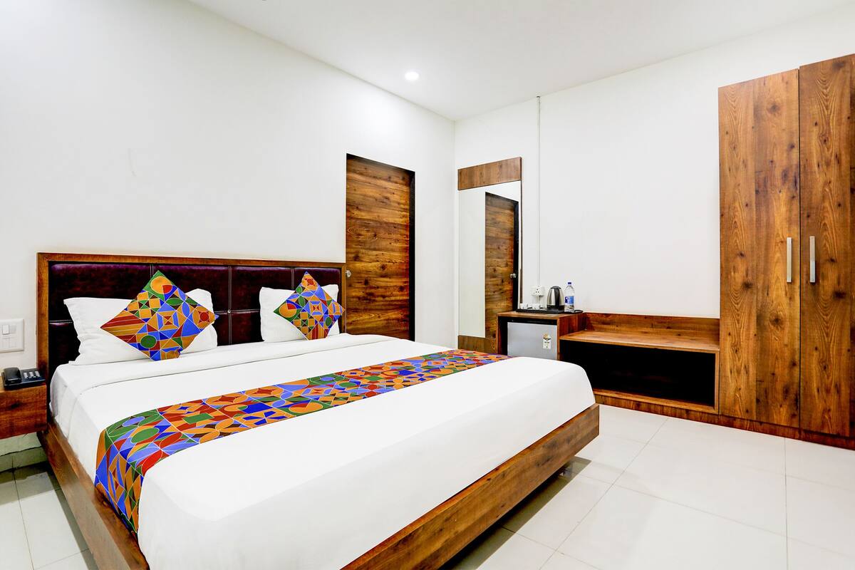 Quarto de hotel com uma cama grande, cabeceira de madeira, uma pequena escrivaninha, um guarda-roupa e um espelho.