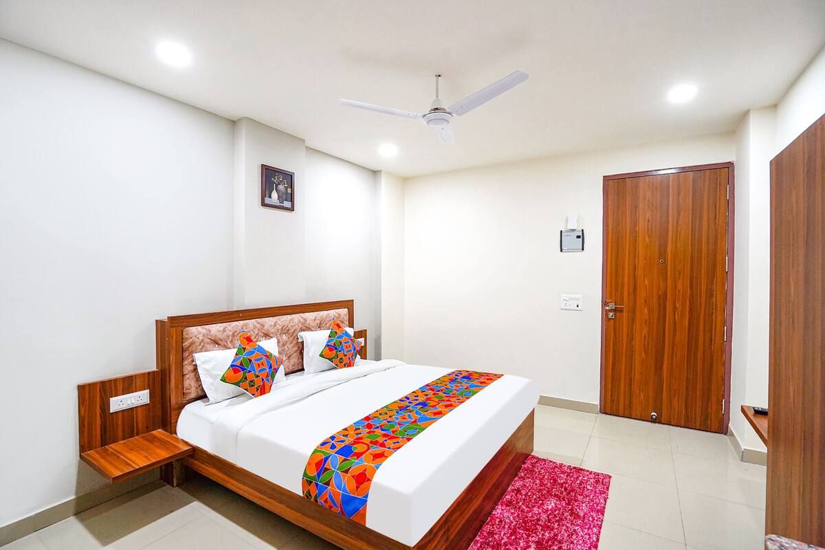 A bedroom with a bed, a wooden headboard, a ceiling fan, a red rug, and a wooden door.