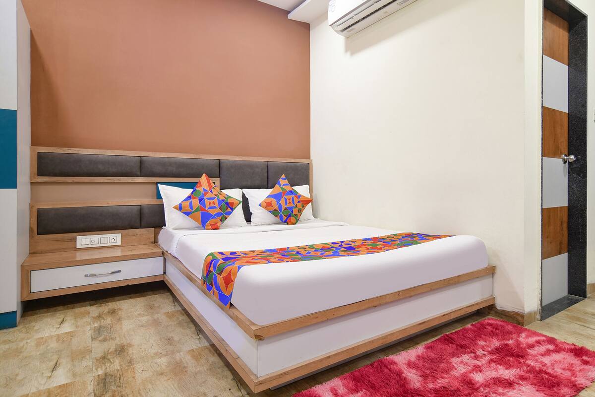 Un dormitorio con cama, mesita de noche, cajón, alfombra roja y unidad de aire acondicionado.