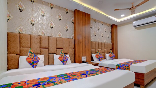 A hotel room with two beds, a wooden headboard, patterned wallpaper, and a ceiling fan. - Fabexpress Sk Prime (Ujjain)