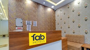 A reception desk with a wooden finish and a logo for 'fab hotels'. There is a sofa and a small table to the right. - Fabexpress Sk Prime (Ujjain)