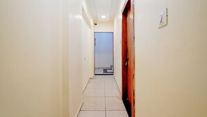 A narrow hallway with white walls and a tiled floor, leading to a door at the end. - Fabexpress Sk Prime (Ujjain)
