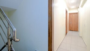 A narrow hallway with a wooden door at the end, a metal railing on the left, and a tiled floor. - Fabexpress Sk Prime (Ujjain)