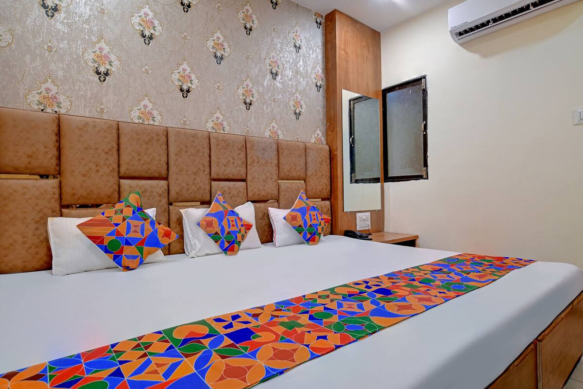 A hotel room with a large bed, a headboard, a mirror, and a patterned wall.