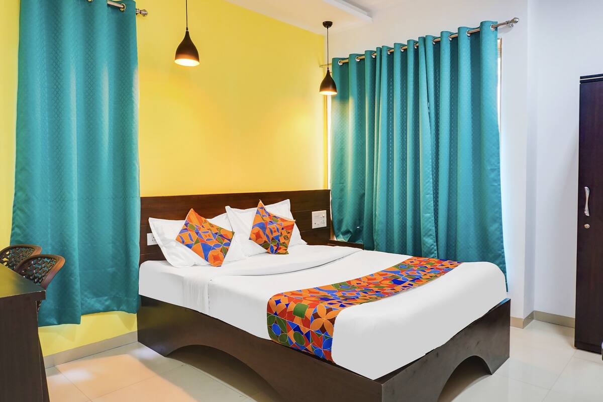 A hotel room with a bed, teal curtains, a wooden headboard, and a bedside table.