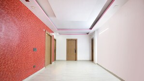A hallway with a red patterned wall, a wooden door, and a light-colored floor. - Fabhotel Capital Inn (Greater Noida)