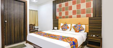A neatly made bed with a colorful geometric-patterned bedspread, a wooden headboard, and a bedside table with a remote control.