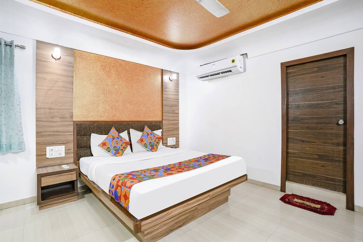 Quarto moderno com cabeceira de madeira, cama com roupa de cama colorida, mesa de cabeceira, tapete vermelho e porta de madeira.