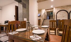 Un comedor con una mesa de mármol, sillas de madera y una escalera al fondo.