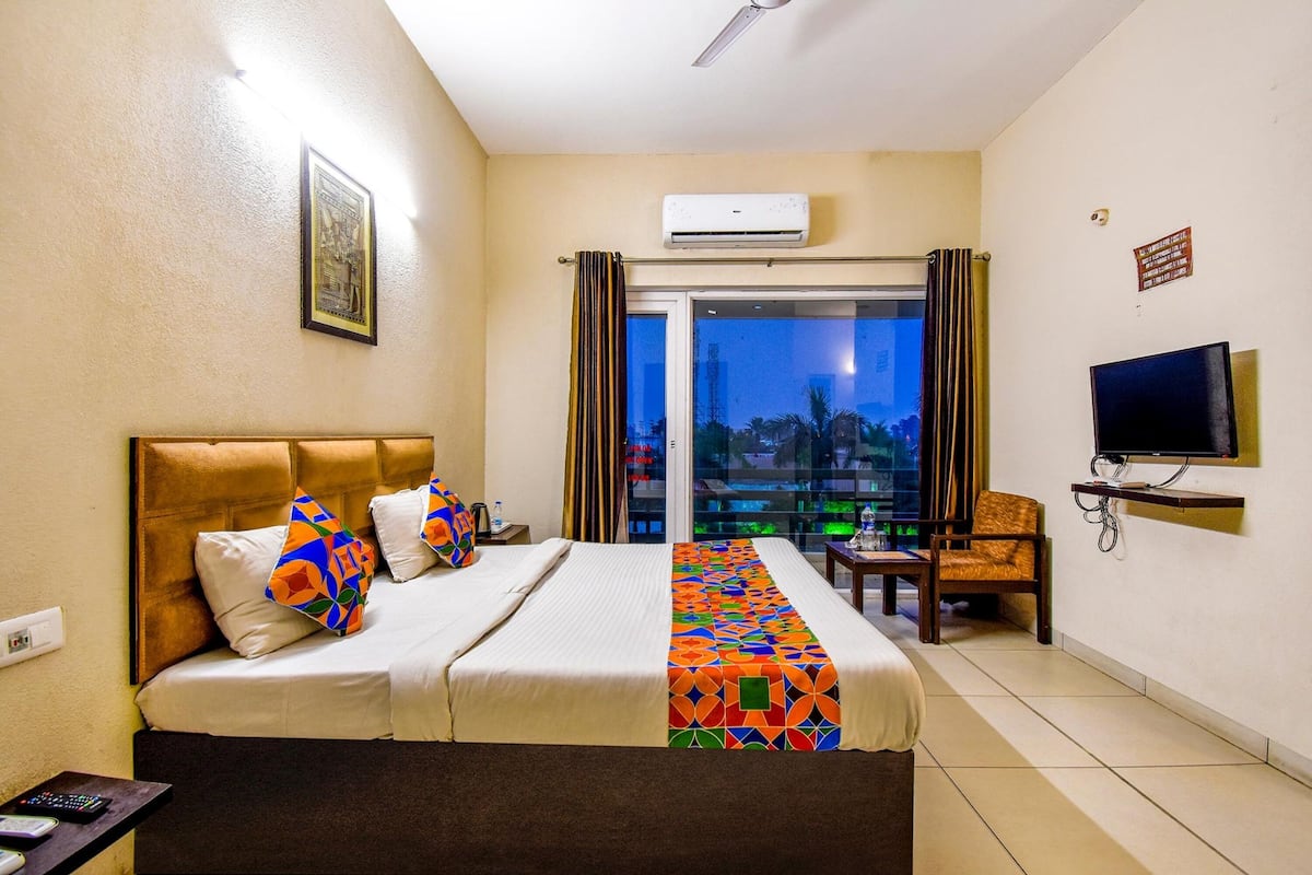 Une chambre d’hôtel avec un lit, une télévision, une chaise et un balcon avec des rideaux.