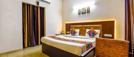 A hotel room with a bed, a chair, an air conditioning unit, a curtain, and a wall-mounted artwork.