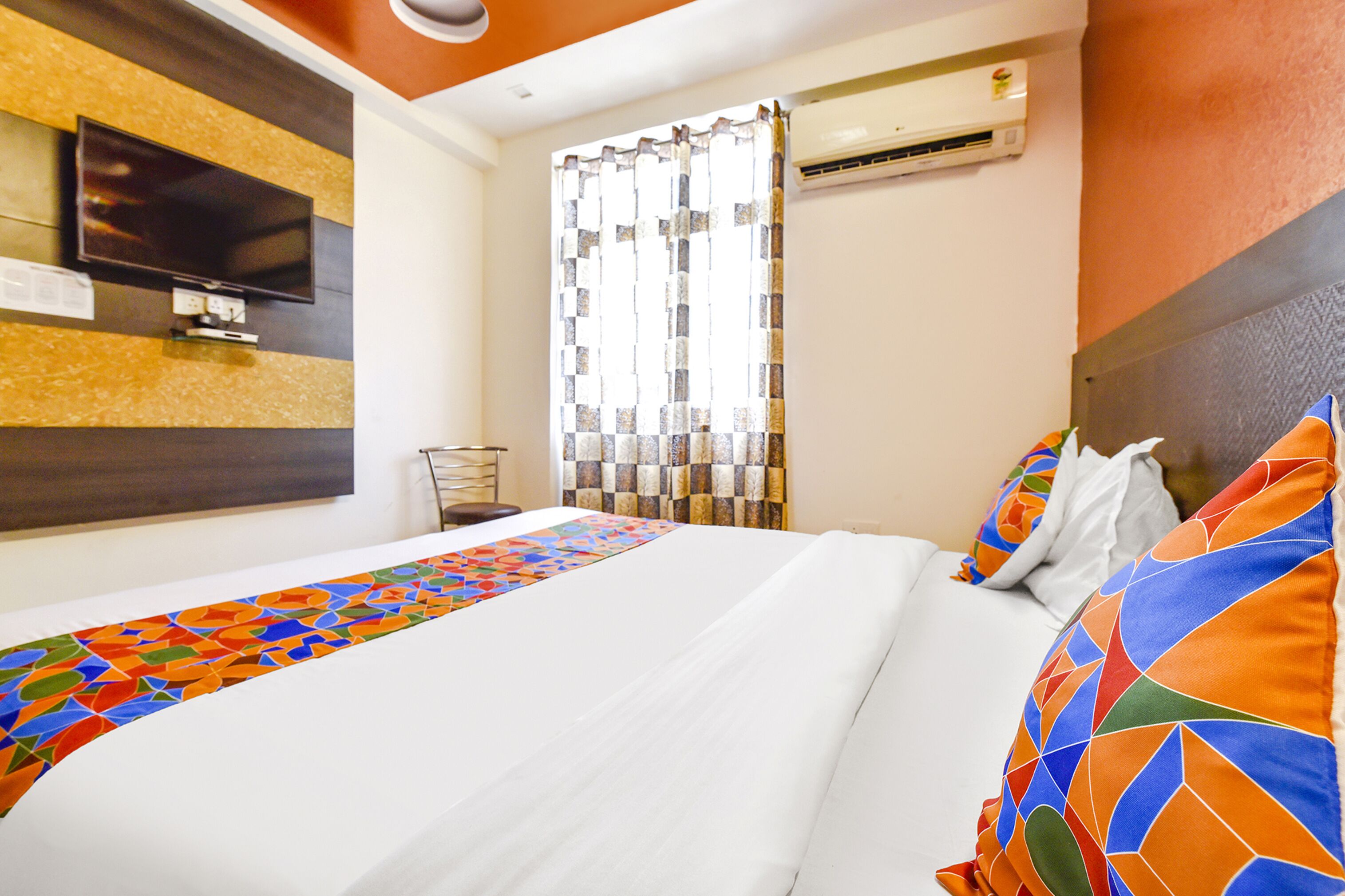 A hotel room with a bed, a TV, an air conditioner, and a window with curtains.
