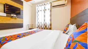 A hotel room with a bed, a TV, an air conditioner, and a window with curtains.