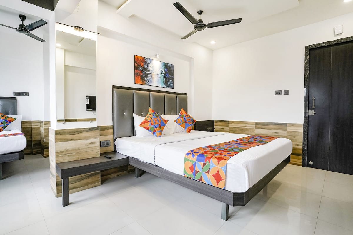 Quarto moderno com cama, mesas de cabeceira, ventoinha no teto e uma porta.
