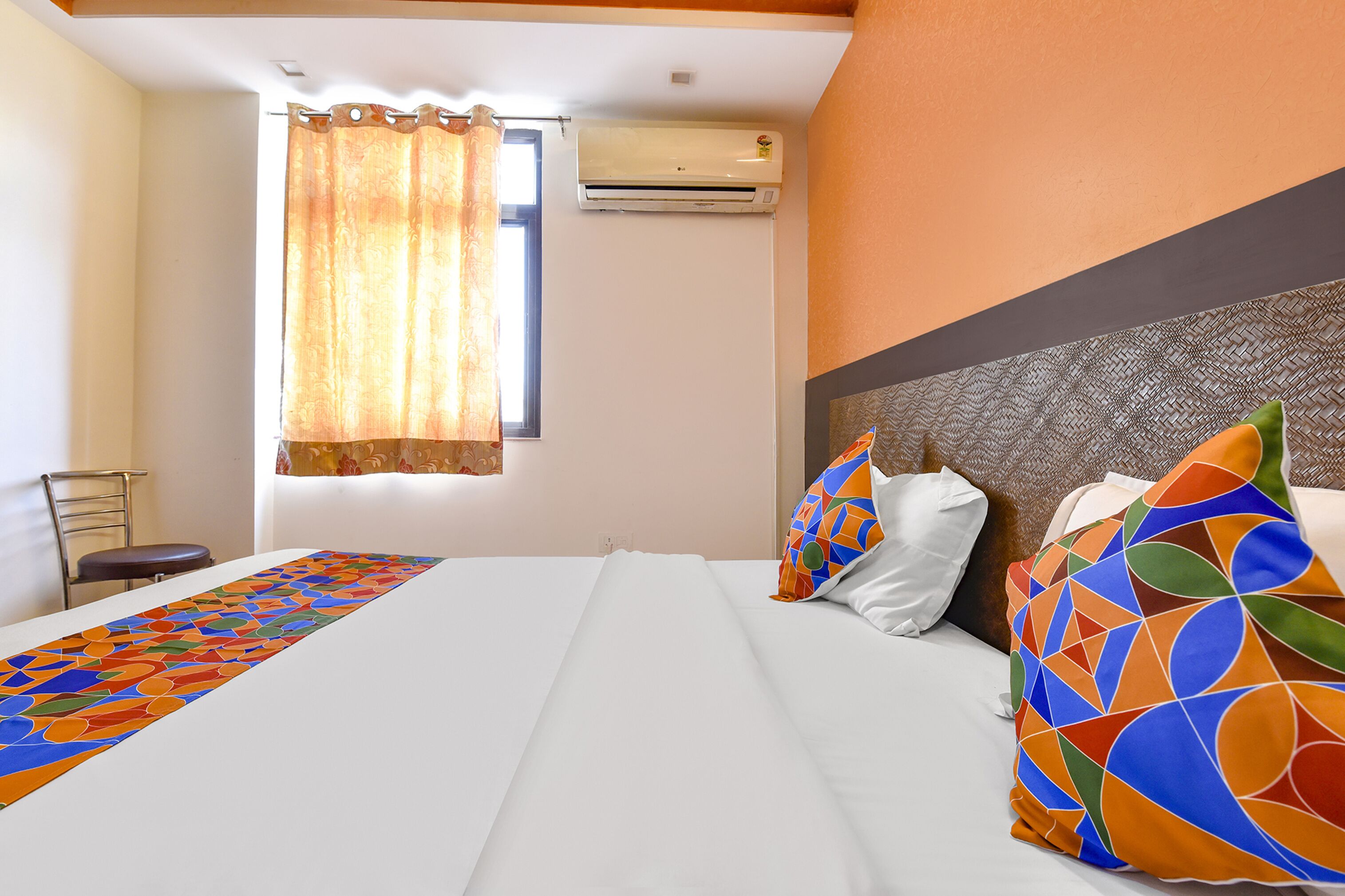 A hotel room with a bed, a window with curtains, an air conditioning unit, and a chair.