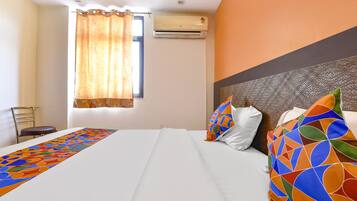 A hotel room with a bed, a window with curtains, an air conditioning unit, and a chair.