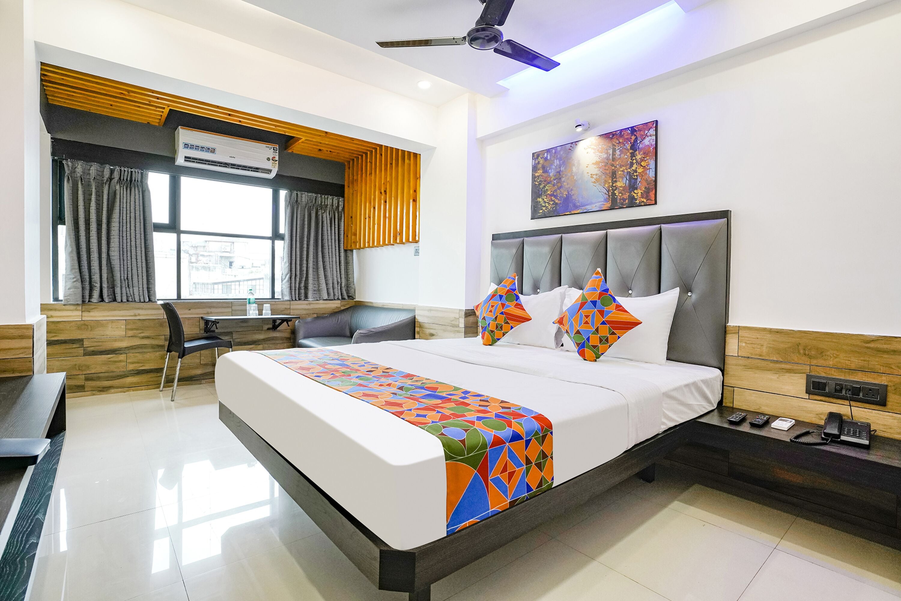 A modern hotel room with a large bed, a desk, and a view of the city.