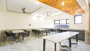 A spacious room with a long table and chairs, a ceiling fan, and a window providing natural light. - FabHotel Prestige Elite (Nashik)