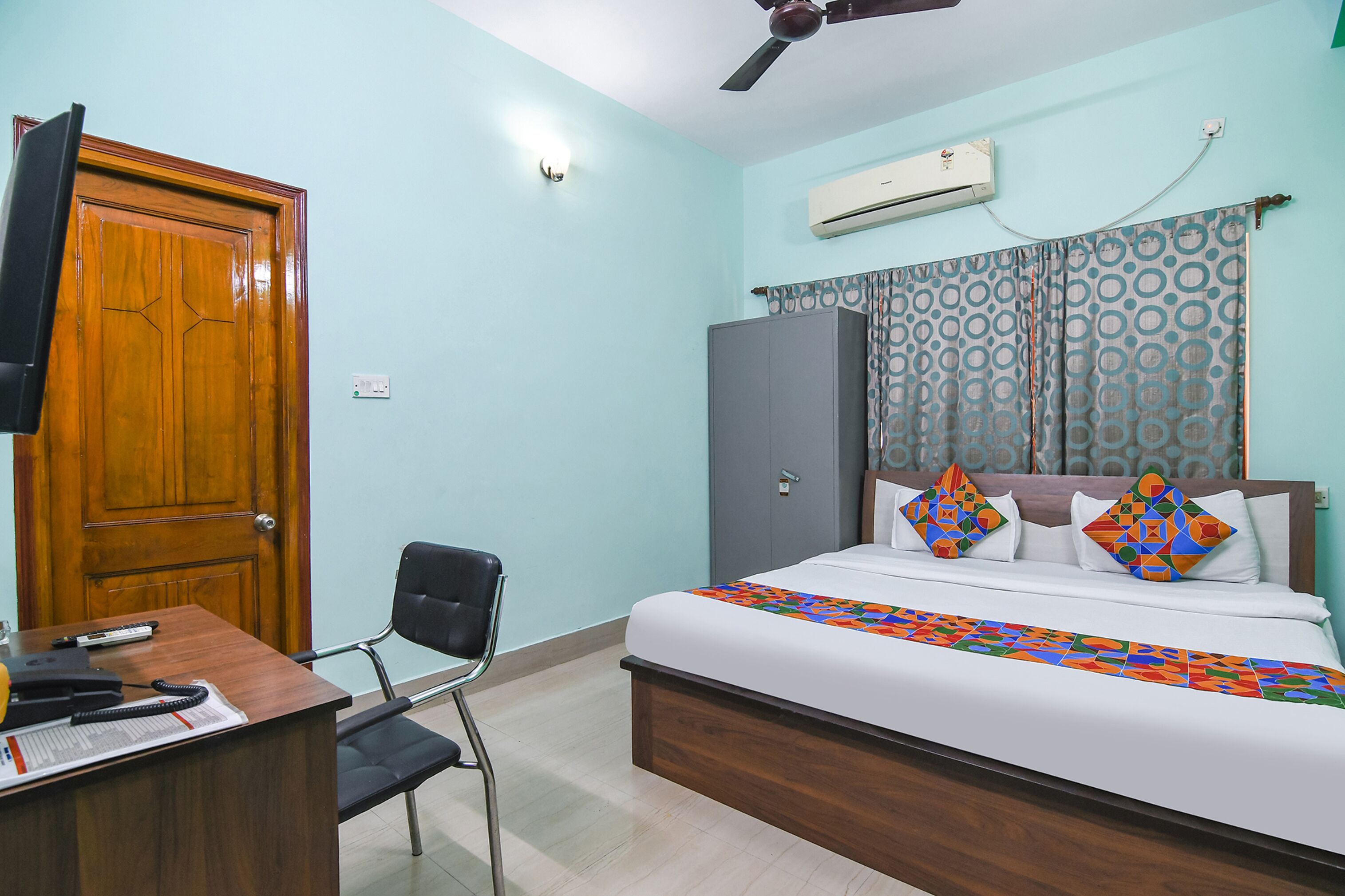 A bedroom with a bed, a desk with a chair, a wardrobe, and a ceiling fan.